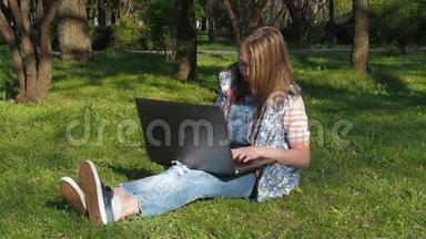 一个十几岁的女孩在草地上的公园里坐着一台电脑。 那个女孩坐在草地上的公园里。 在公园里阳光明媚的一天